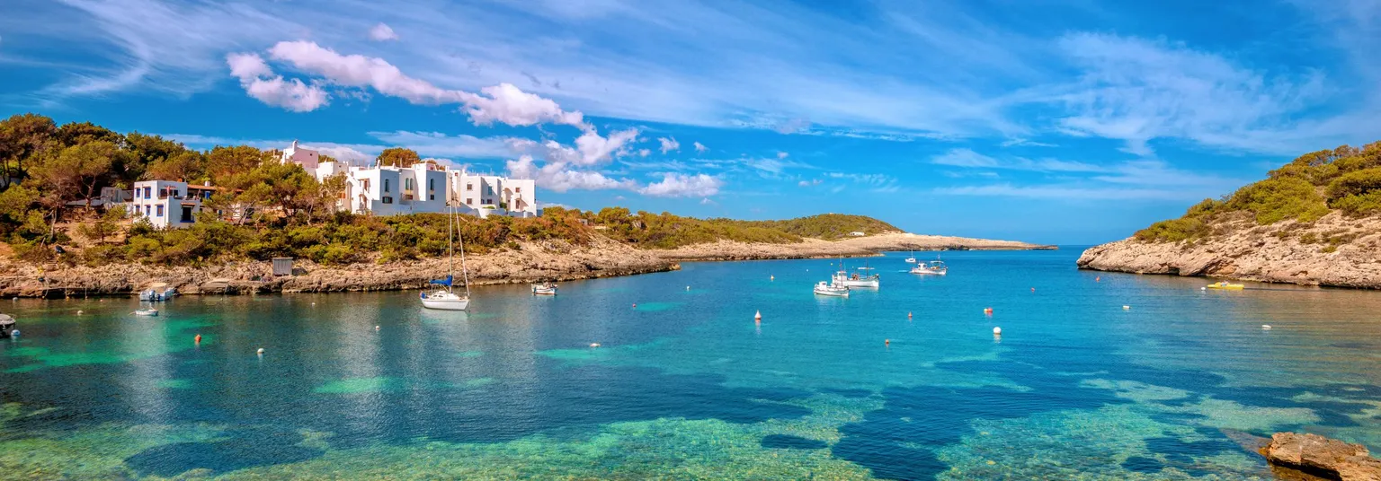 Een blauwe baai in Ibiza met op de achtergrond witte Spaanse huisjes.
